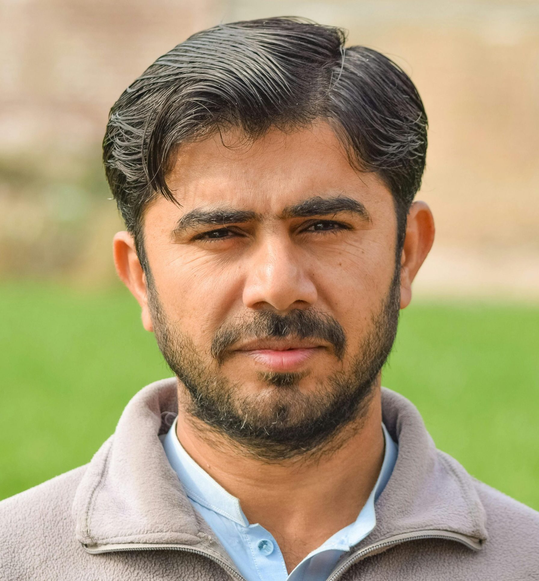 Close-up portrait of a bearded man in a field, looking directly at the camera.