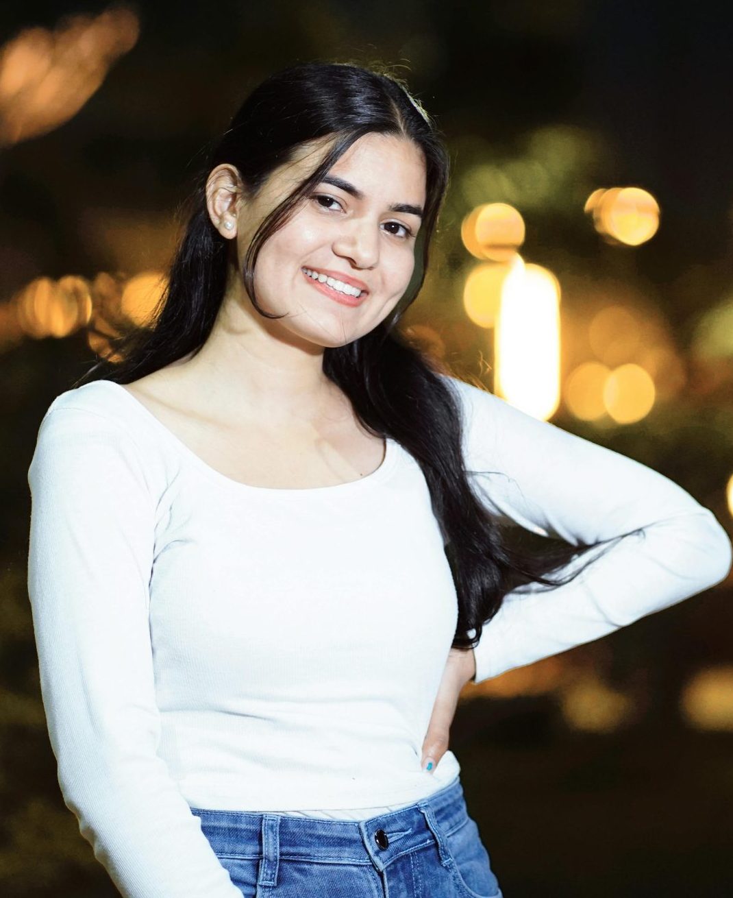 Smiling woman poses in a nighttime cityscape with blurred lights.